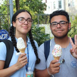 Two people holding up peace signs and eating ice cream.