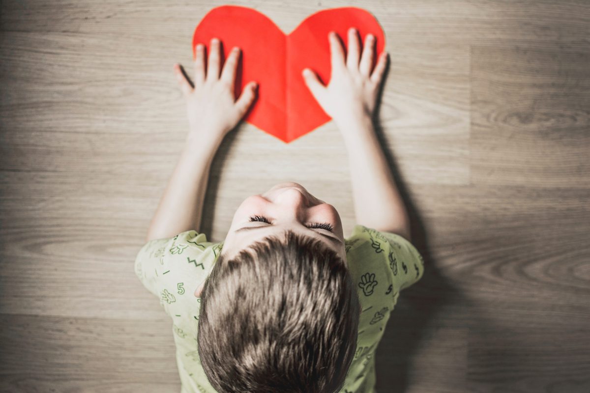 A boy is holding up a paper heart.